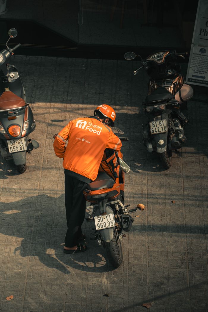 Delivery person in orange jacket with motorbike from above view.